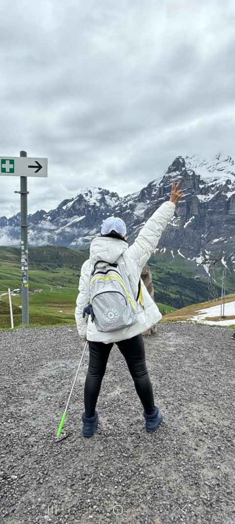 Person in a winter jacket with a backpack, pointing at a mountain landscape.