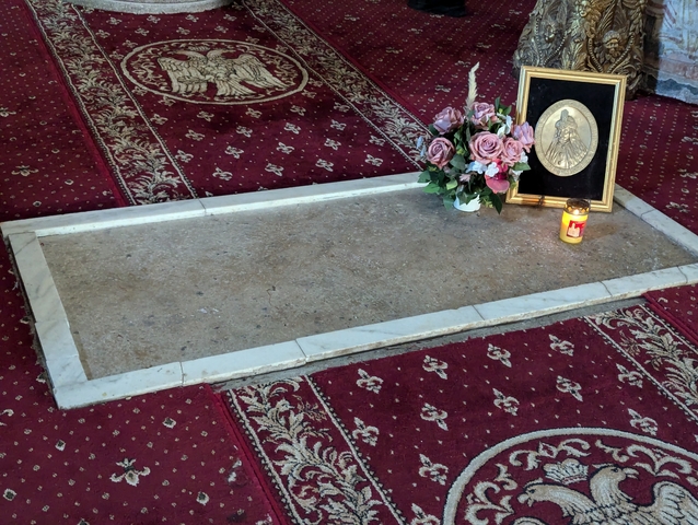       Gravestone with flowers and a candle on a red carpet.
  