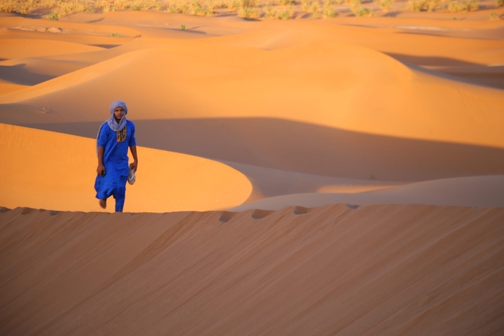 Person in traditional attire on sand dunes.