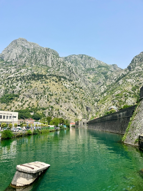       River and fortress wall with dramatic mountain backdrop.
  