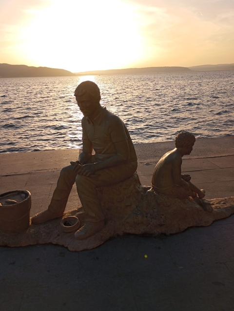 Bronze statues of a man and child by the sea during sunset.