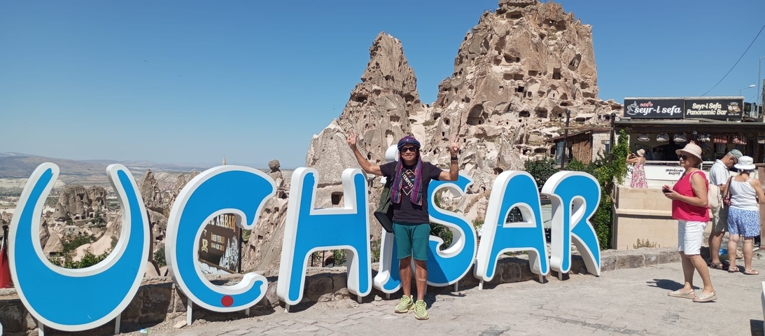       Two people posing in front of Uchisar Castle sign in Cappadocia, Turkey.
  