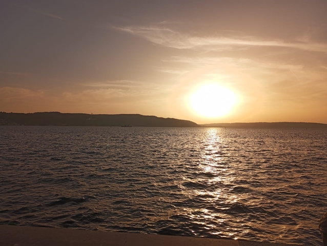       Sunset over water with a silhouette of a landmass.
  