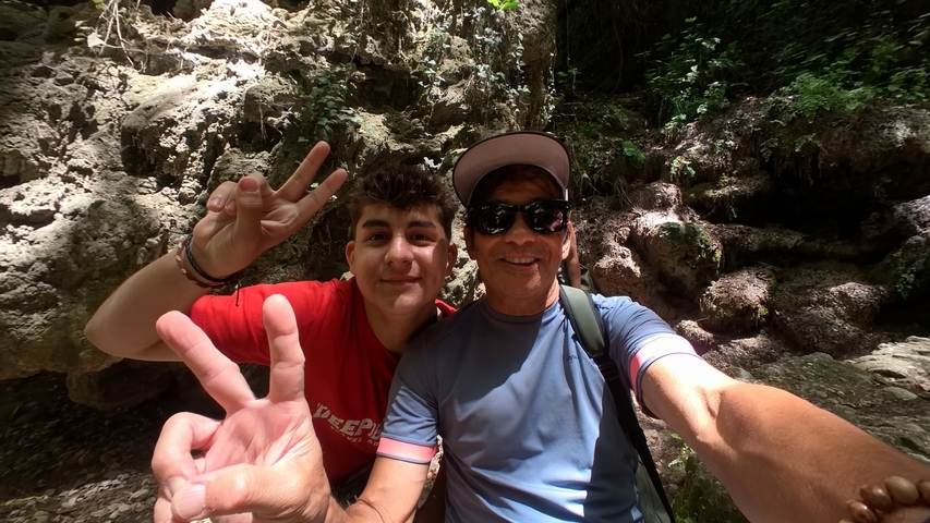 Two people posing with peace signs in front of a rocky wall.