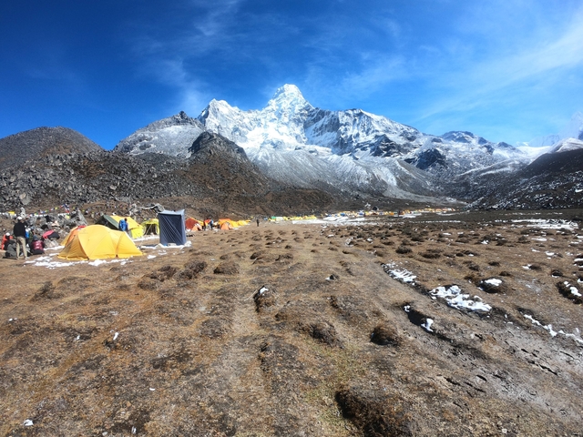       Camp with bright tents in a snow and rocky Himalayan landscape.
  