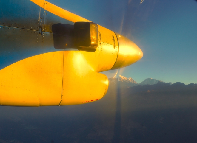       Close-up of a yellow airplane propeller with mountain range in the background.
  
