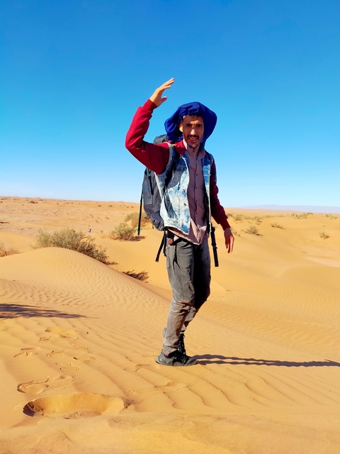       Person walking in a desert carrying a backpack.
  