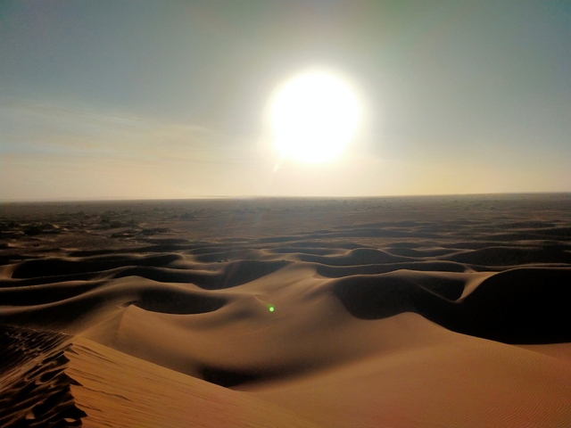       Desert landscape with sun setting over the dunes.
  