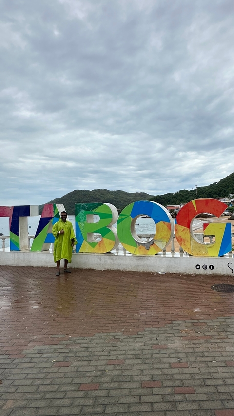       Person standing in front of colorful letters spelling 'TABOGA' with the sea in the background.
  