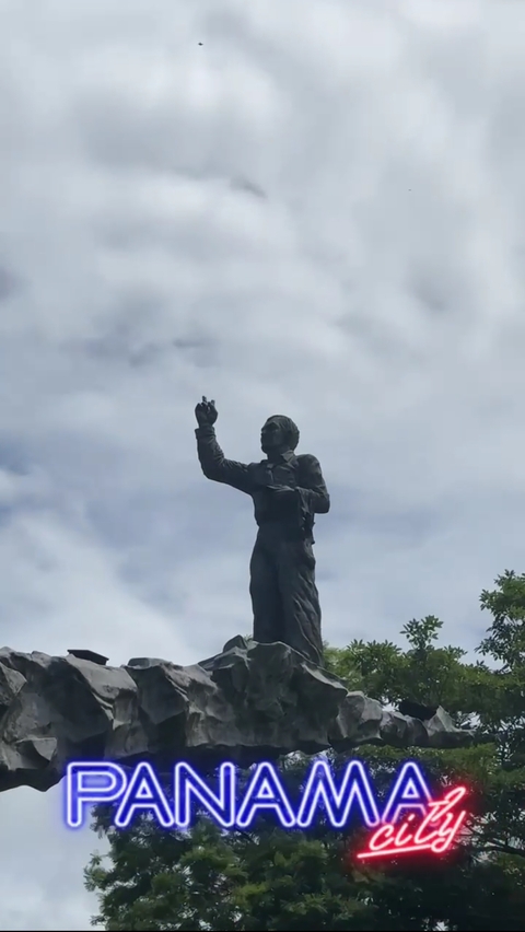       Statue of a person pointing upwards against a cloudy sky.
  