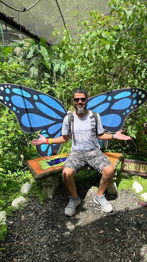       Man seated in front of decorative butterfly wings in a garden.
  