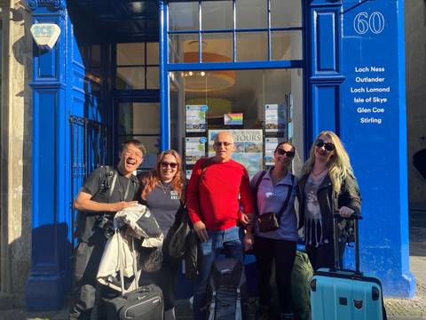       Group of people posing in front of a blue building with travel signs.
  