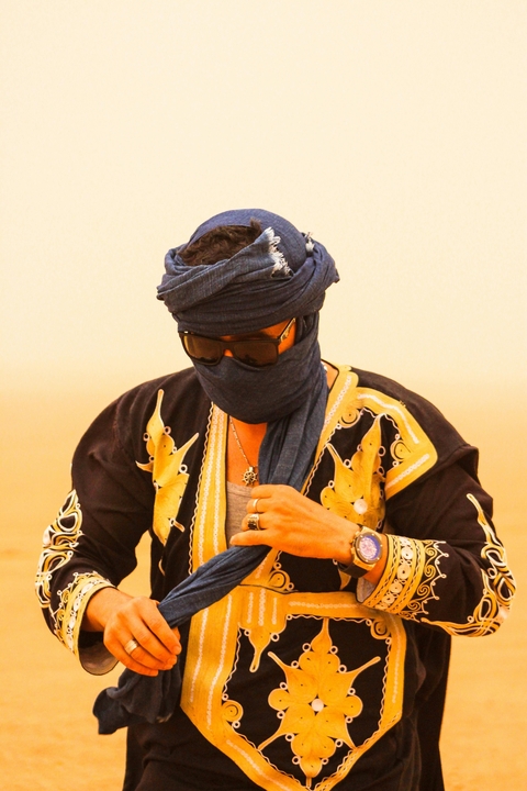 Person in traditional attire and sunglasses in a desert setting.