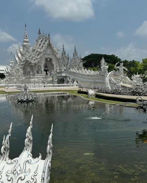 White intricately designed temple with a pond in front.