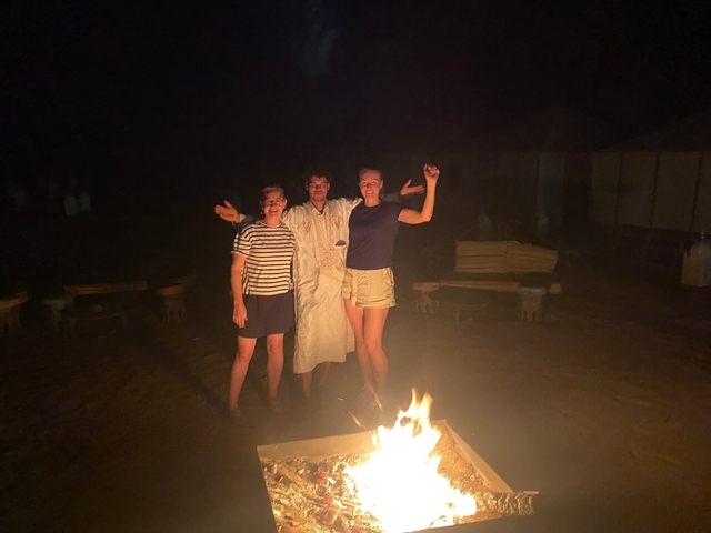       Three people posing by a campfire at night.
  