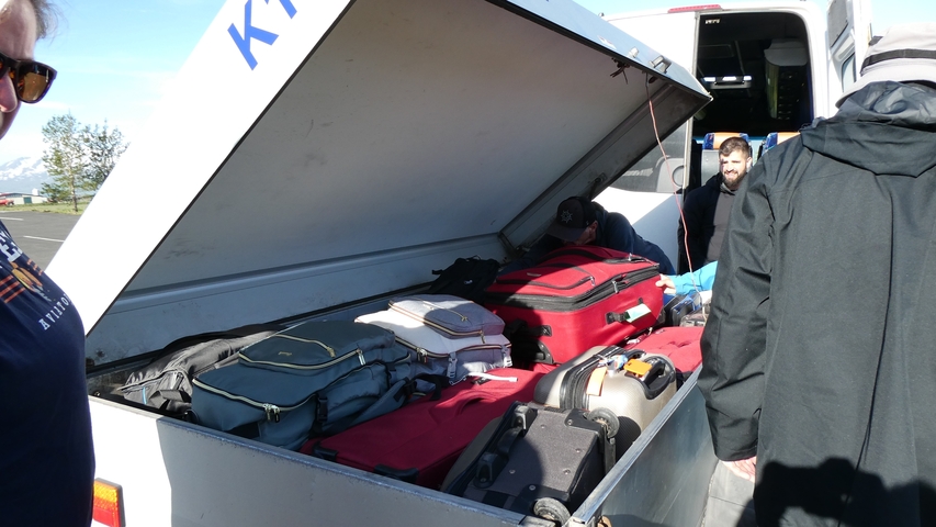       Travelers arranging luggage into a storage compartment.
  