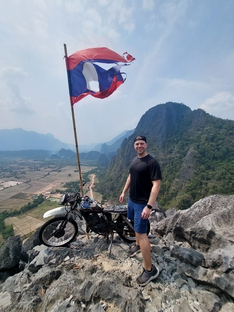 Traveler poses with a flag atop a hill offering panoramic views.