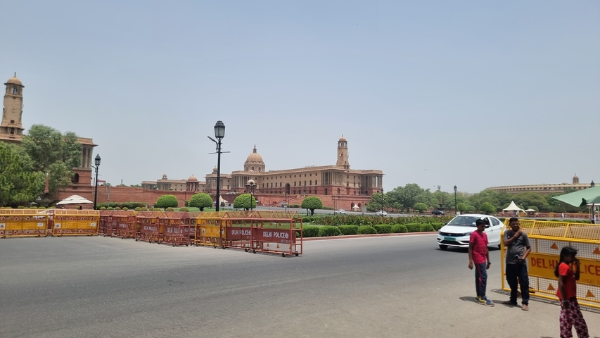 Image of people standing next to a road with famous Indian architecture in the background.