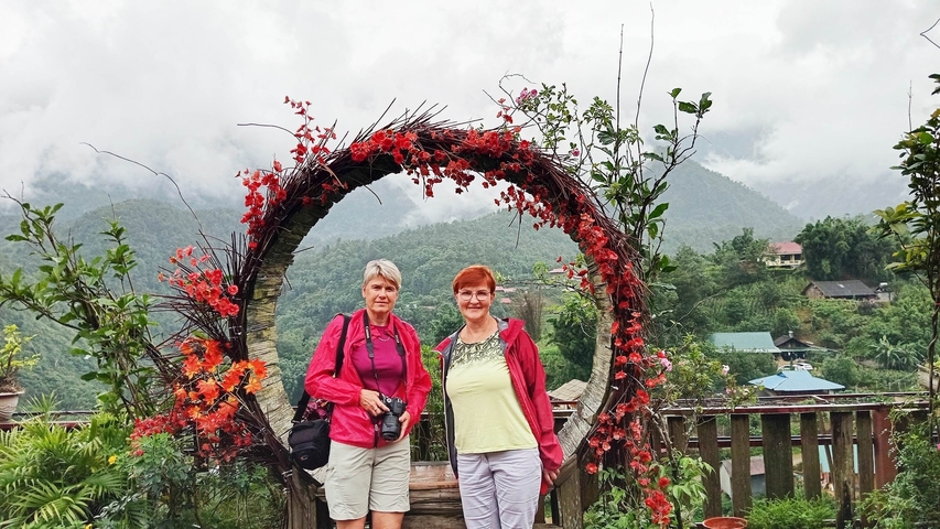       Two people posing in front of a circular decoration with scenic mountainous background.
  