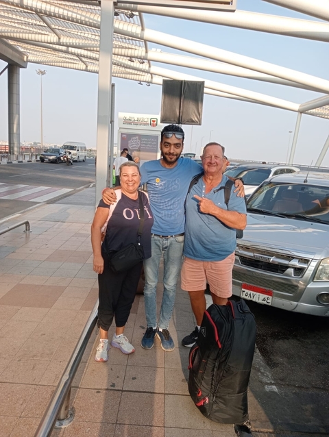       Three people posing in an outdoor setting with a vehicle.
  