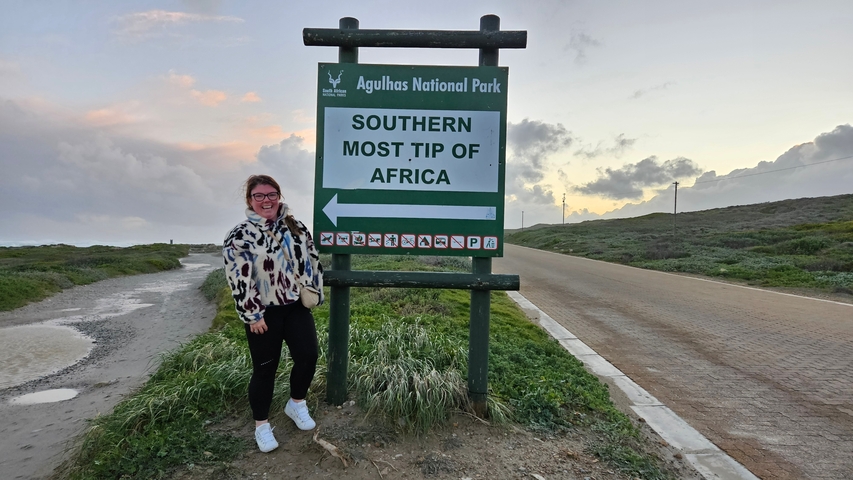       A person standing next to a sign indicating the southernmost tip of Africa.
  