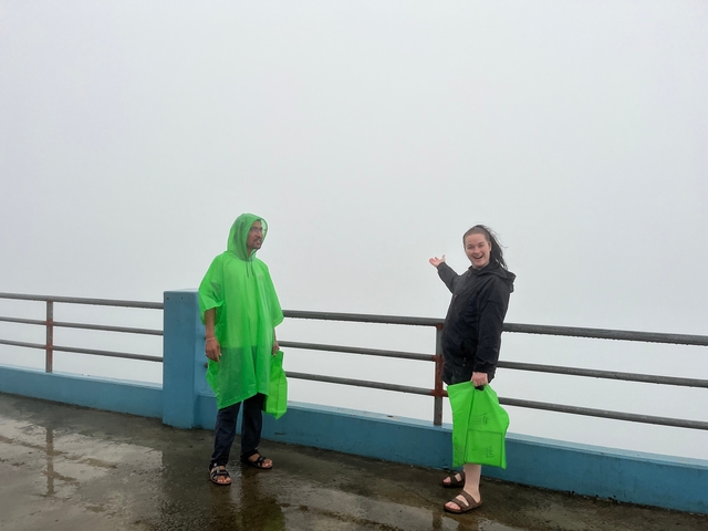       Two people in raincoats on a misty overlook.
  