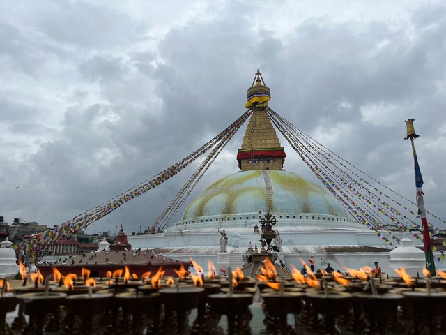       Boudhanath Stupa with prayer flags under cloudy sky.
  