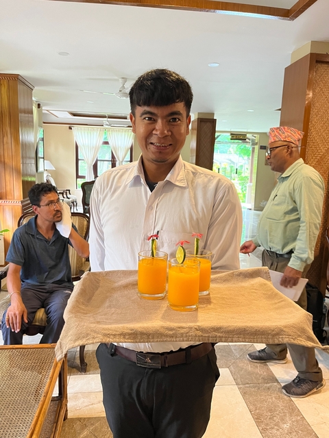       Smiling waiter serving orange drinks on a tray.
  