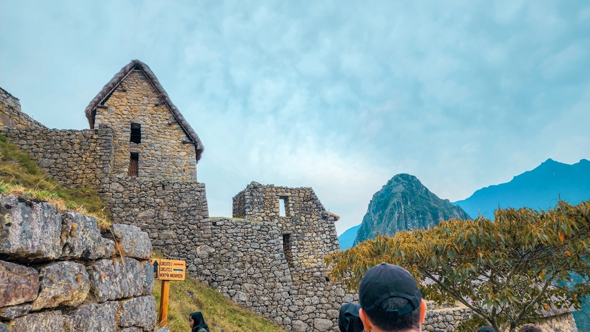       Tourists near stone ruins with Machu Picchu mountain in the background.
  