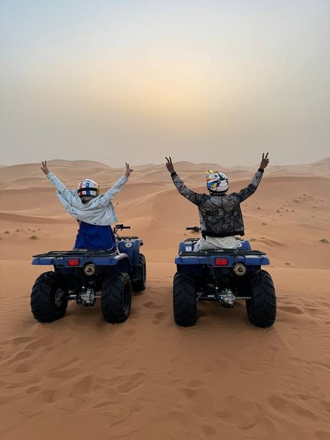 Two people on quad bikes with arms raised in celebration in the desert.