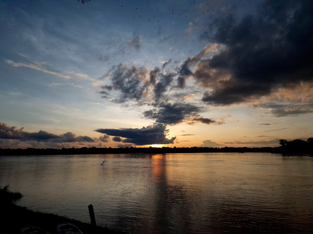 Sunset view over a calm river with dramatic clouds.
