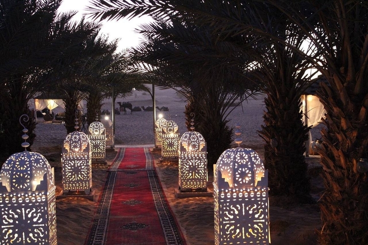 Desert camp with decorative lanterns and palm trees at dusk.