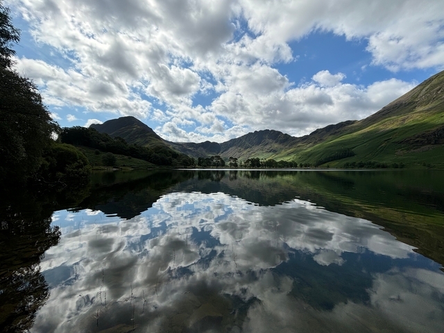 Serene lake with mountain reflections and cloudy sky.