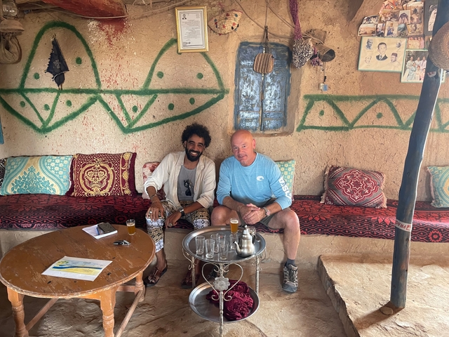 Two men enjoying traditional Moroccan tea in an interior with colorful cushions.