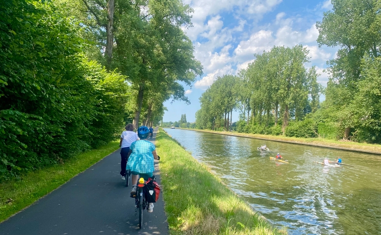 Cyclists riding along a canal with trees lining the path.