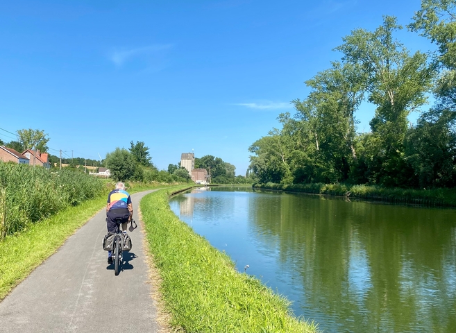 Cyclist along a canal path with clear blue skies.
