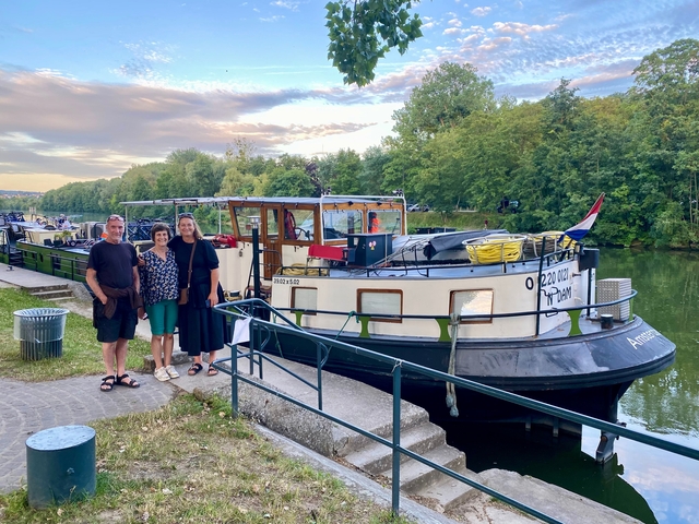 Three people standing in front of a boat on a canal.