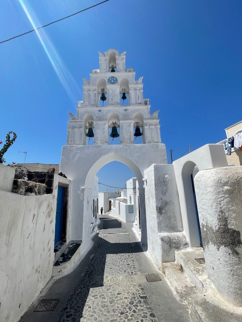 White-washed buildings with archways and a bell tower against a clear blue sky.