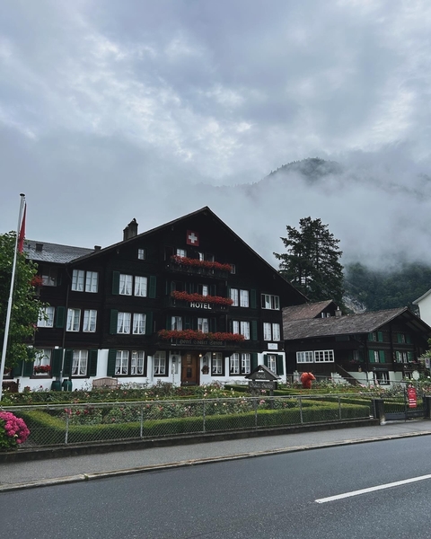 Traditional wooden hotel with Swiss flag and misty mountain backdrop.
