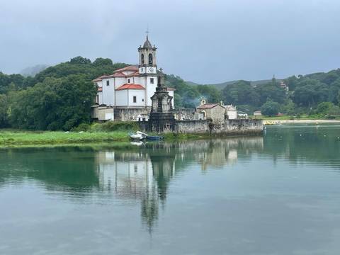       Historic church with a clock tower reflected in water.
  