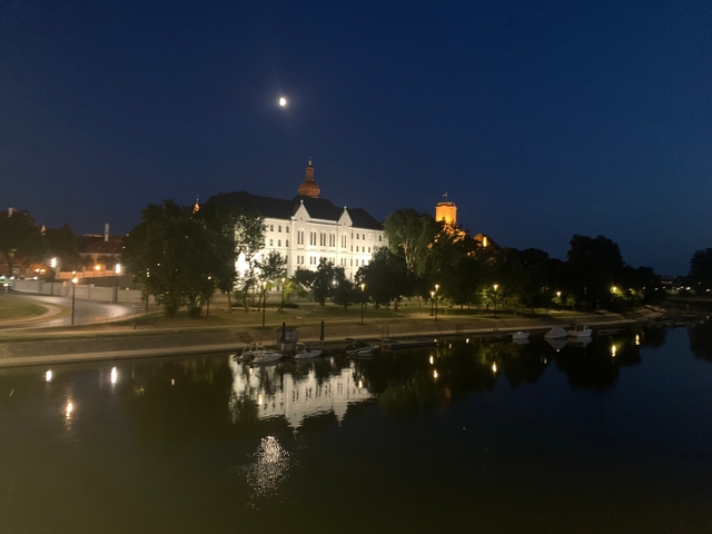 Buildings reflected in a river at night with a full moon above.