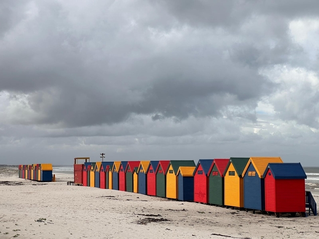 Colorful beach huts lined up along a beach under a cloudy sky.