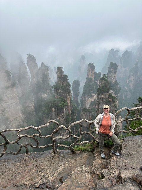       Person posing in front of misty mountains with unique rock formations.
  