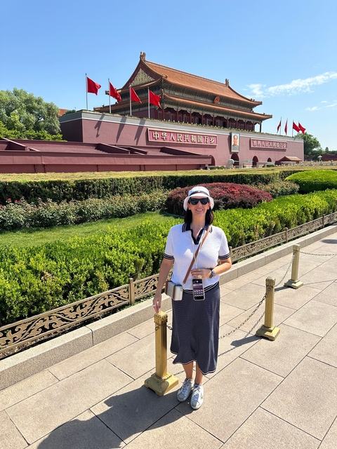 A woman in sunglasses and a hat standing in front of a large red wall with Chinese characters.