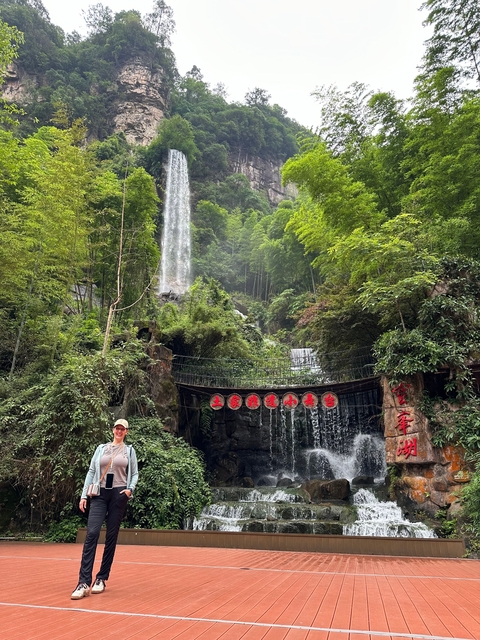 A man standing in front of a lush green waterfall surrounded by trees.