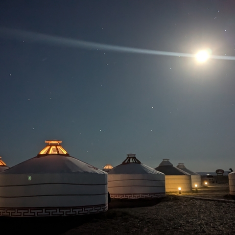       Night sky with bright moon above traditional yurts.
  