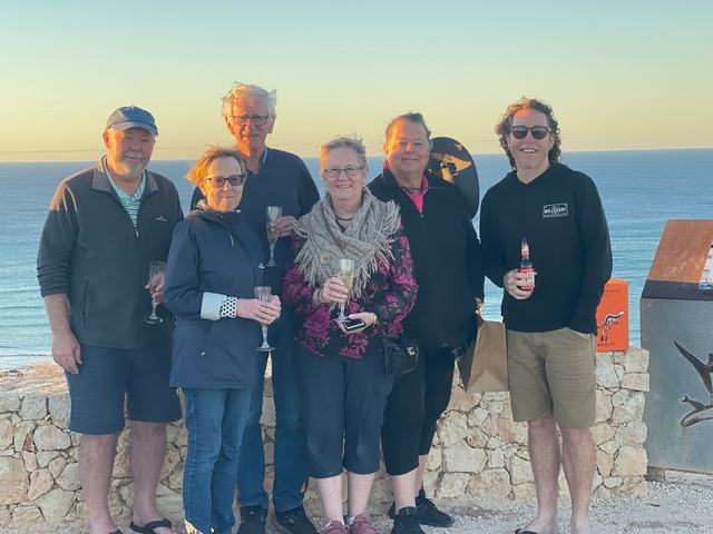 Group of people posing with drinks by the ocean.