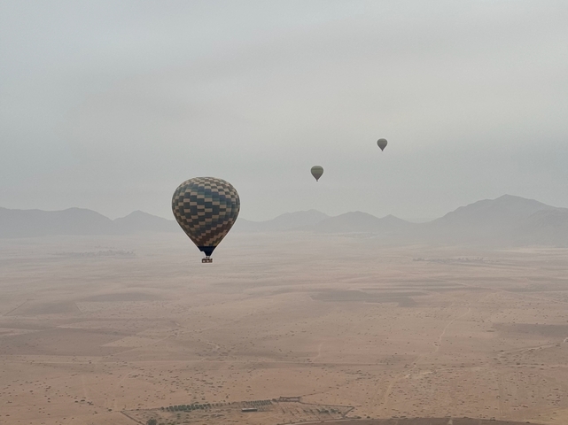       Hot air balloons floating over a desert with mountains in the background.
  