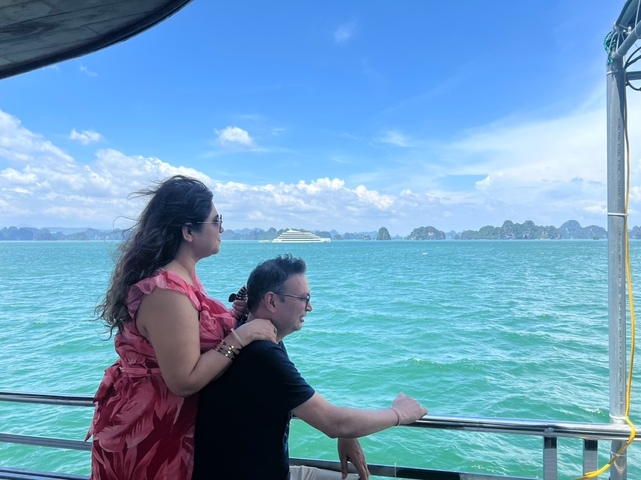 Couple on a boat enjoying a scenic view of the ocean with a cruise ship in the distance.