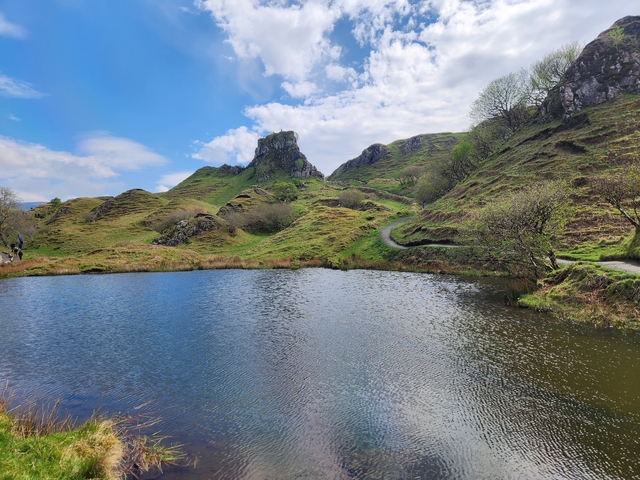 Green hills, a lake, and a rocky structure in scenic nature.